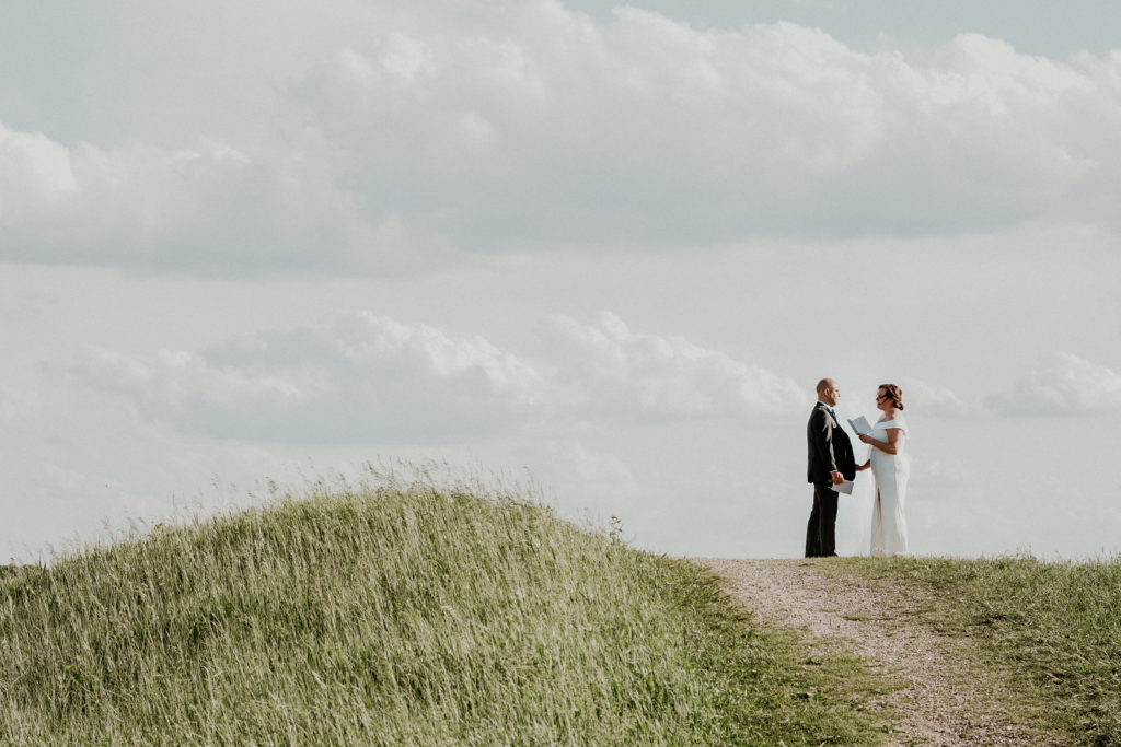 Bride + groom holding hands and exchanging elopement vows by themselves outside on a hill
