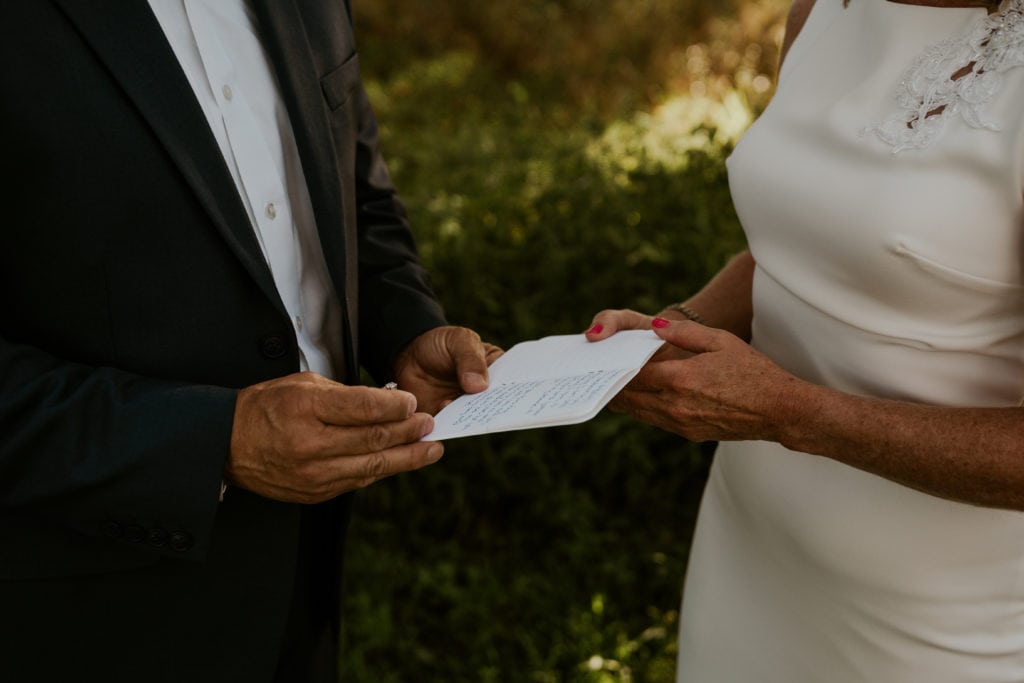 groom reads his elopement vows while holding a wedding band and vow book