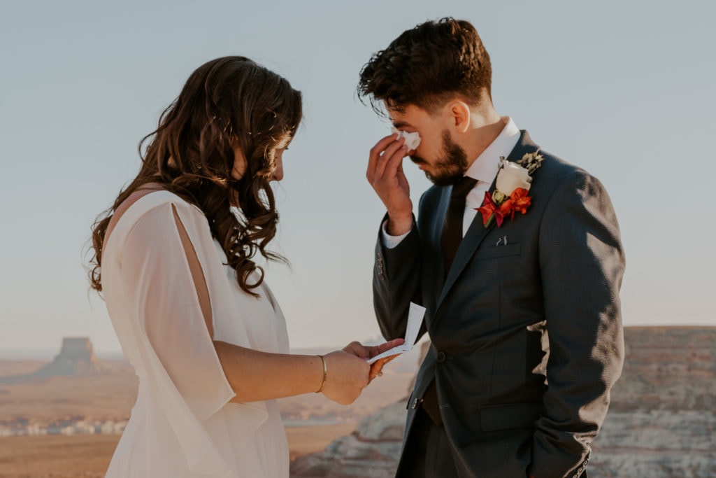 Bride and groom tearfully reading letters from family at their elopement ceremony in Lake Powell, Utah